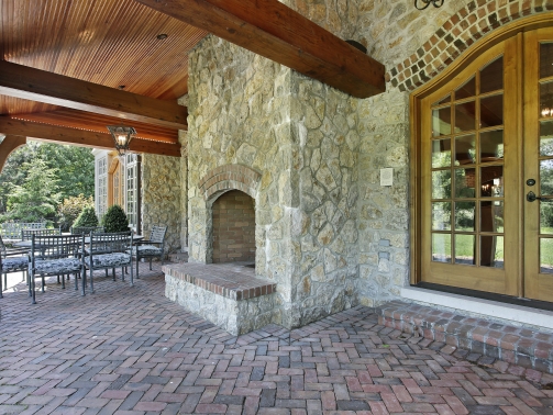 Brick patio outside luxury home with stone fireplace